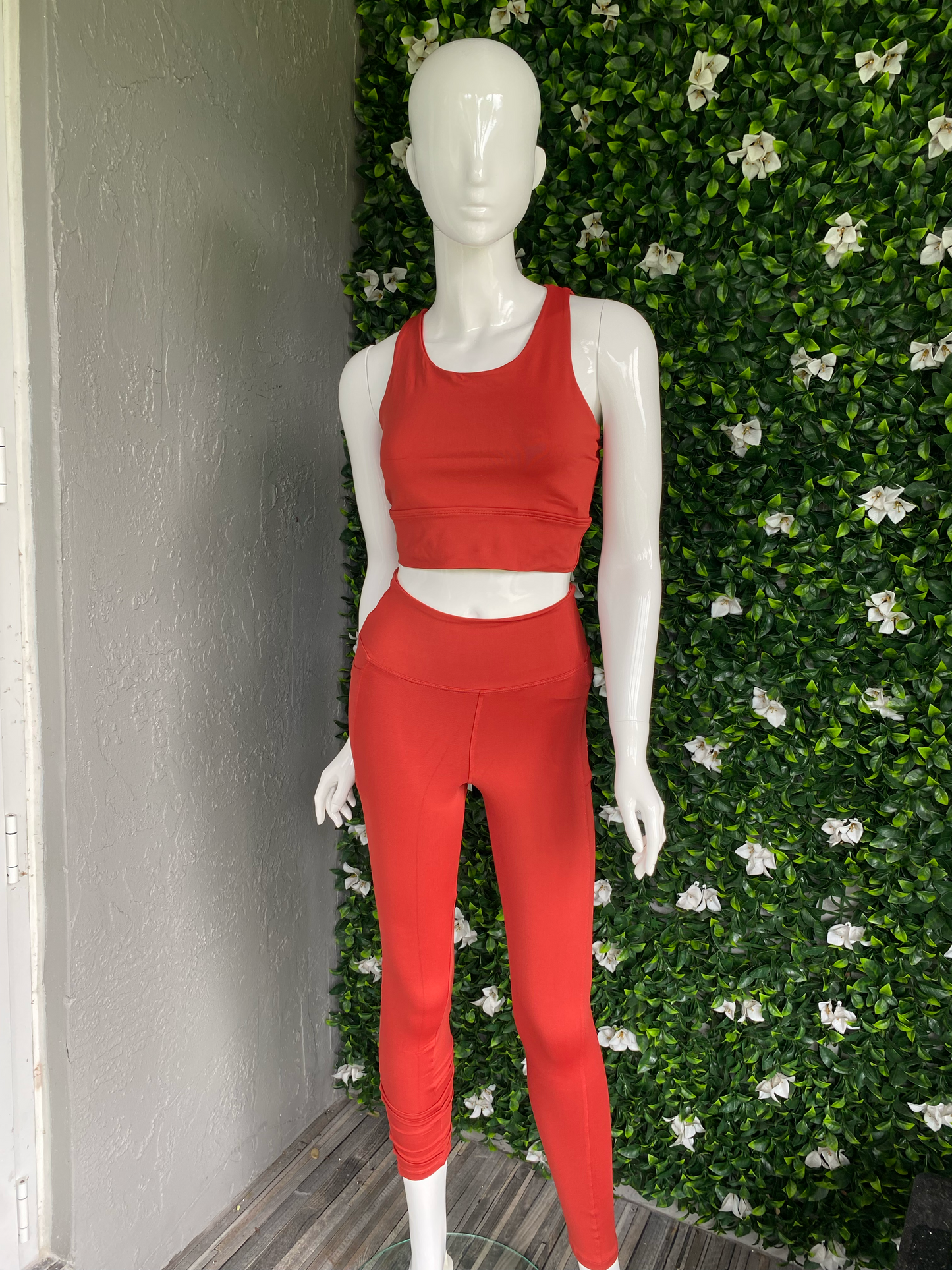 Mannequin wearing a red outfit against a green and white floral background